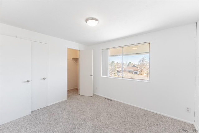 unfurnished bedroom with visible vents, a walk in closet, baseboards, carpet floors, and a closet