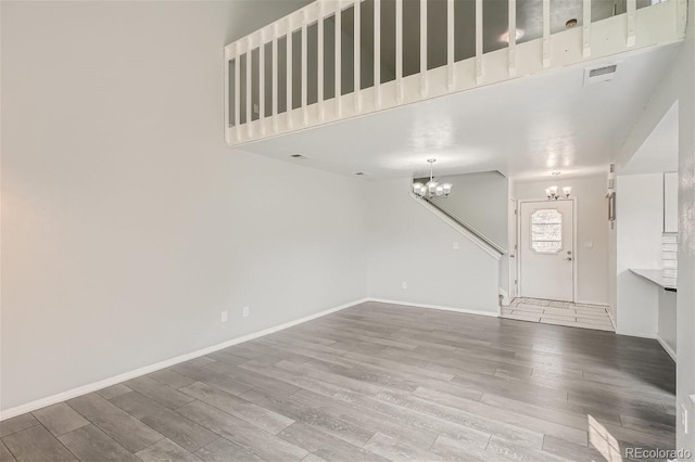 unfurnished living room featuring visible vents, baseboards, a notable chandelier, and wood finished floors