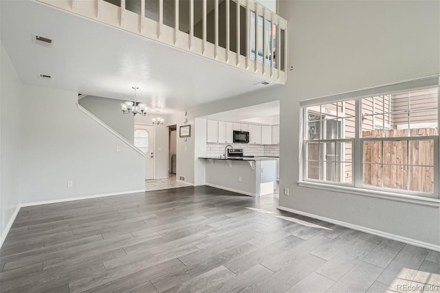 unfurnished living room with visible vents, baseboards, a chandelier, a high ceiling, and wood finished floors