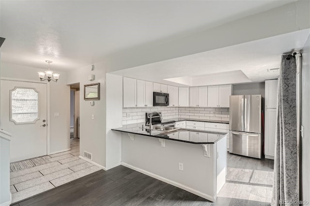 kitchen featuring visible vents, a peninsula, wood finished floors, stainless steel appliances, and a sink