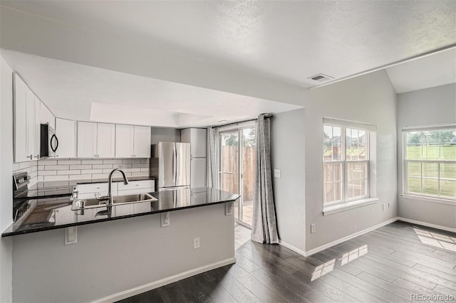 kitchen with visible vents, backsplash, appliances with stainless steel finishes, a peninsula, and dark wood-style flooring