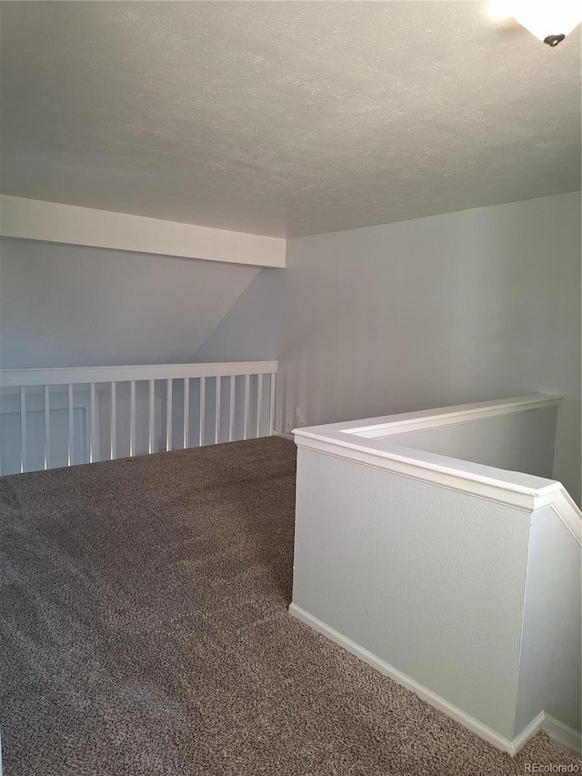 hallway featuring lofted ceiling, carpet, baseboards, and a textured ceiling