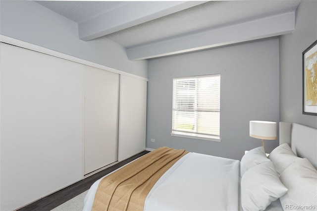 bedroom featuring dark wood-type flooring, beam ceiling, and a textured ceiling