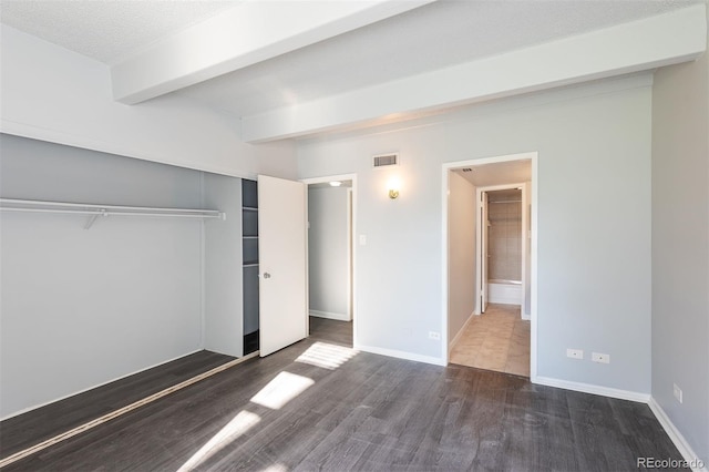 unfurnished bedroom with beam ceiling, dark wood-type flooring, a closet, connected bathroom, and a textured ceiling