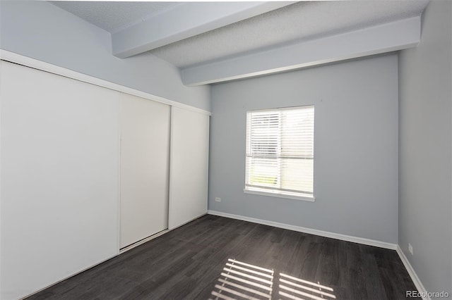 empty room featuring beamed ceiling, dark wood-type flooring, and a textured ceiling