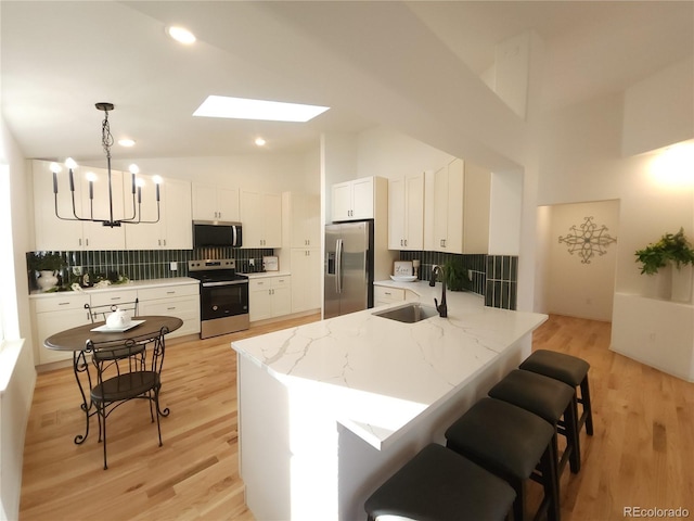 kitchen with a kitchen bar, a peninsula, stainless steel appliances, white cabinetry, and a sink