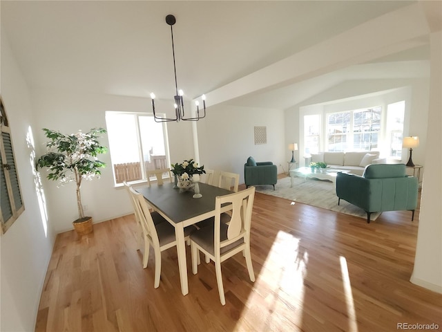 dining room featuring a chandelier, a healthy amount of sunlight, light wood finished floors, and lofted ceiling