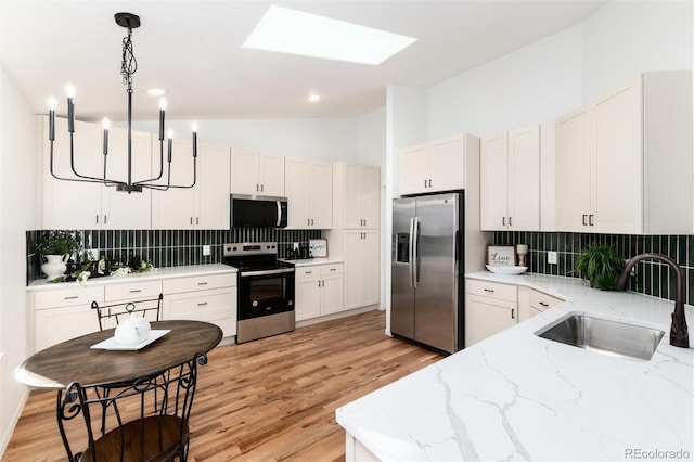 kitchen featuring backsplash, light stone countertops, pendant lighting, stainless steel appliances, and a sink