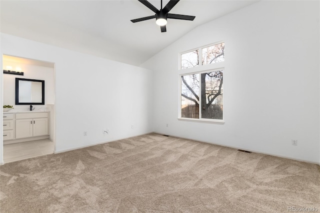 unfurnished bedroom featuring high vaulted ceiling, light colored carpet, ensuite bathroom, and a sink