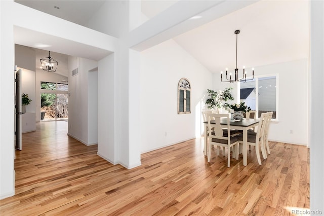 dining room with light wood finished floors, a notable chandelier, high vaulted ceiling, and visible vents