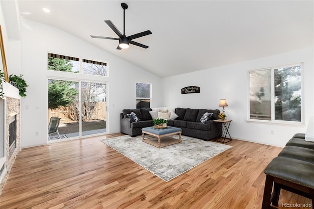 living area featuring a fireplace, high vaulted ceiling, light wood-type flooring, and a ceiling fan