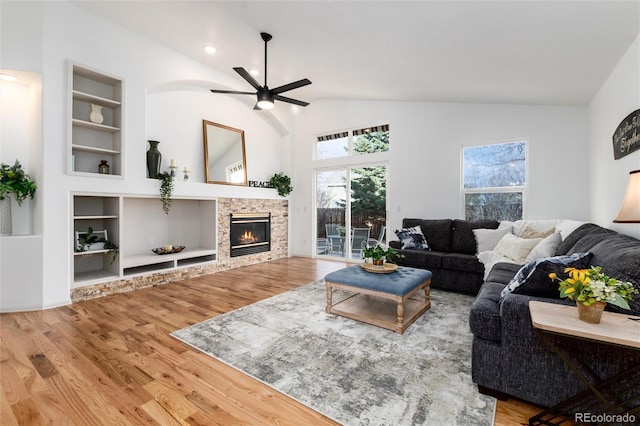 living room with built in shelves, a ceiling fan, wood finished floors, a fireplace, and lofted ceiling