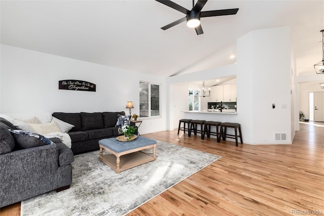 living room with visible vents, ceiling fan with notable chandelier, high vaulted ceiling, and light wood-style floors