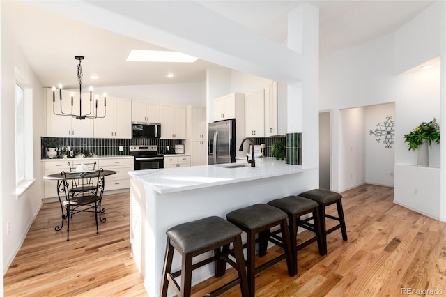 kitchen with a breakfast bar area, appliances with stainless steel finishes, a notable chandelier, white cabinets, and a sink