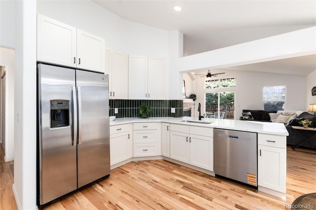 kitchen featuring a sink, open floor plan, stainless steel appliances, a peninsula, and light countertops