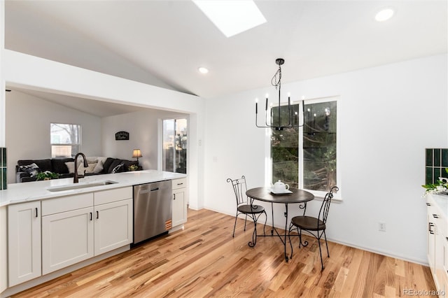 kitchen featuring light wood-type flooring, vaulted ceiling with skylight, a sink, dishwasher, and open floor plan