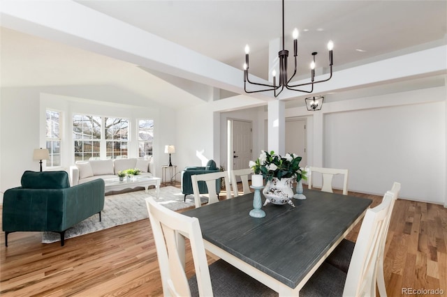 dining space with light wood finished floors, lofted ceiling, and an inviting chandelier