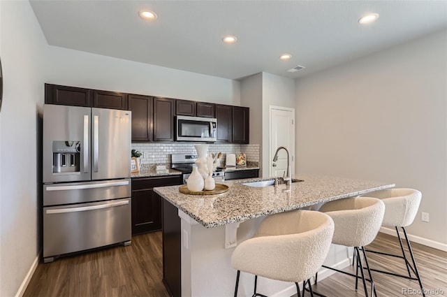 kitchen featuring sink, a breakfast bar, stainless steel appliances, tasteful backsplash, and an island with sink