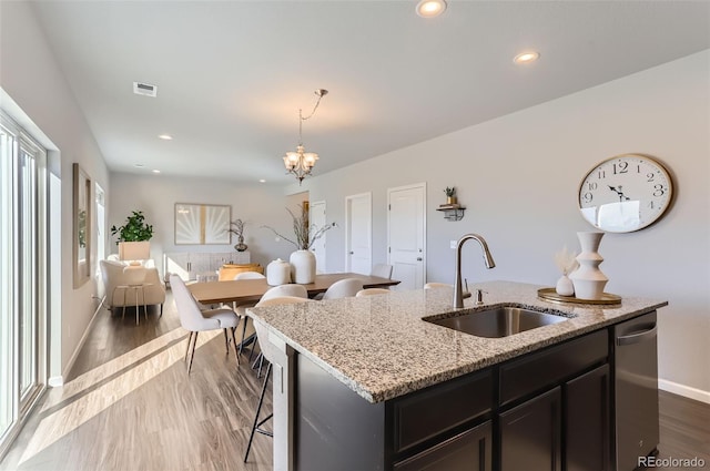 kitchen featuring dark wood-type flooring, sink, light stone counters, hanging light fixtures, and a center island with sink