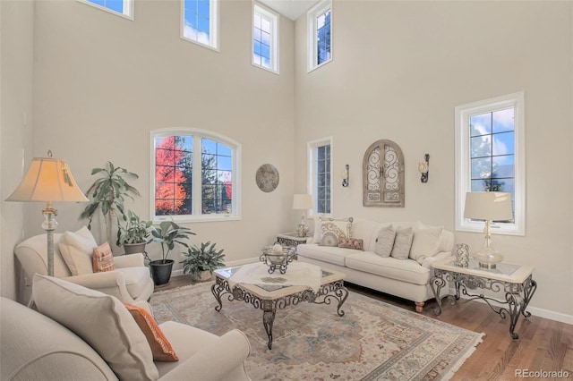 living room with a wealth of natural light, baseboards, wood finished floors, and a towering ceiling