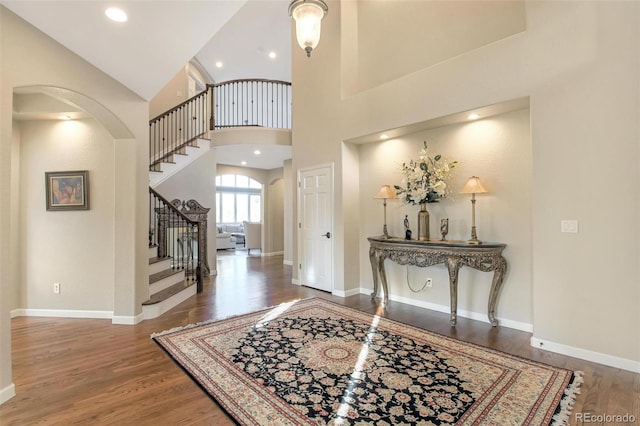 foyer with baseboards, a towering ceiling, wood finished floors, arched walkways, and stairway