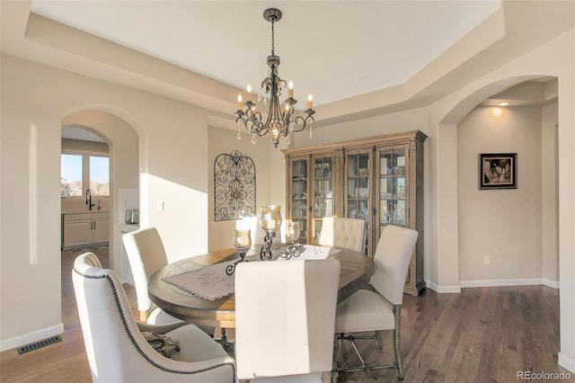 dining area featuring an inviting chandelier, visible vents, wood finished floors, and arched walkways