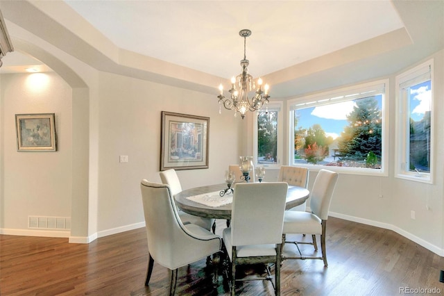 dining area featuring a tray ceiling, dark wood-style flooring, arched walkways, and an inviting chandelier
