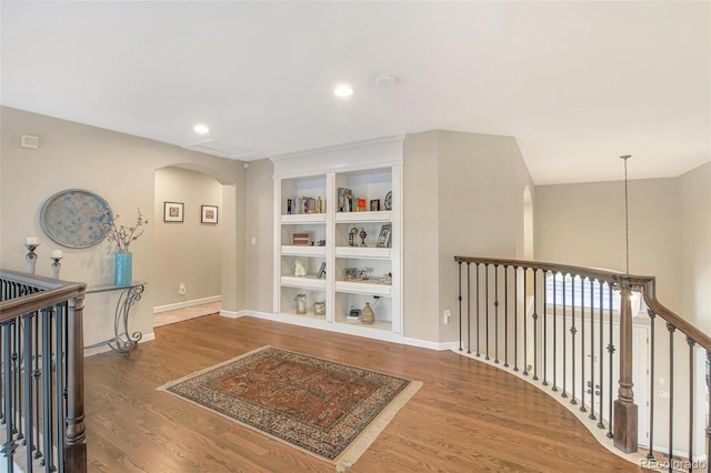 hall featuring built in features, wood finished floors, baseboards, and arched walkways