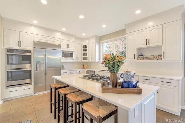 kitchen with built in appliances, white cabinetry, a kitchen breakfast bar, and a center island