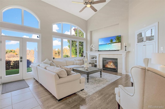 living area with french doors, high vaulted ceiling, ceiling fan, light wood finished floors, and a tile fireplace