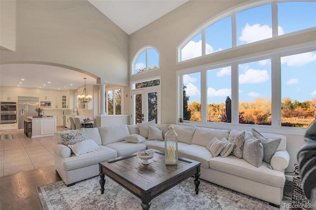living room with an inviting chandelier, high vaulted ceiling, arched walkways, light wood-style floors, and ornate columns
