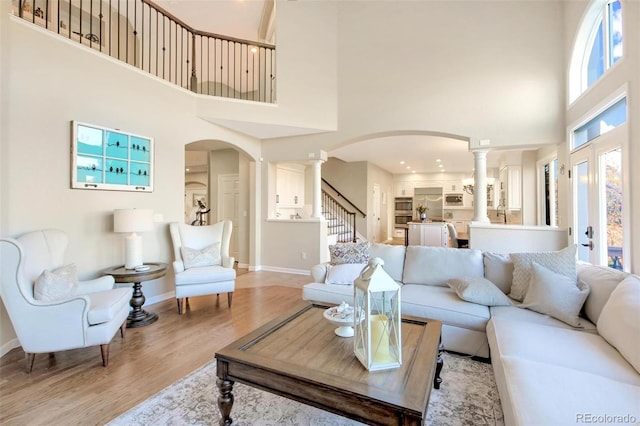 living room with a high ceiling, light wood finished floors, stairs, arched walkways, and ornate columns