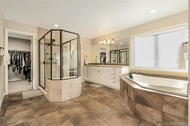 bathroom featuring a garden tub, a stall shower, a notable chandelier, vanity, and a spacious closet