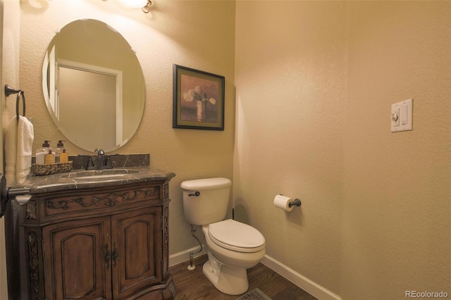half bath with toilet, baseboards, wood finished floors, and vanity