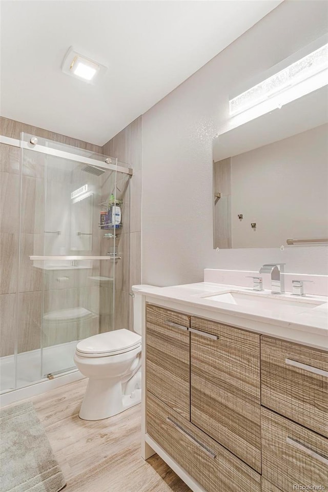 bathroom with hardwood / wood-style floors, vanity, toilet, and walk in shower