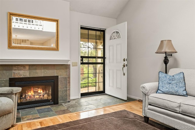 entryway with wood finished floors, vaulted ceiling, baseboards, and a fireplace
