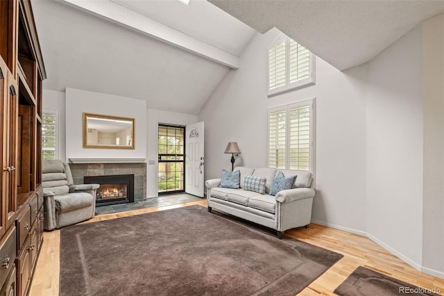living area featuring beam ceiling, a tile fireplace, wood finished floors, high vaulted ceiling, and baseboards