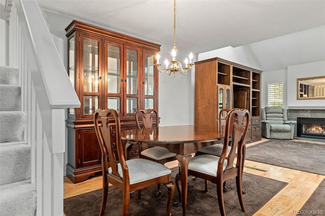 dining space with a chandelier, stairway, wood finished floors, a tile fireplace, and vaulted ceiling