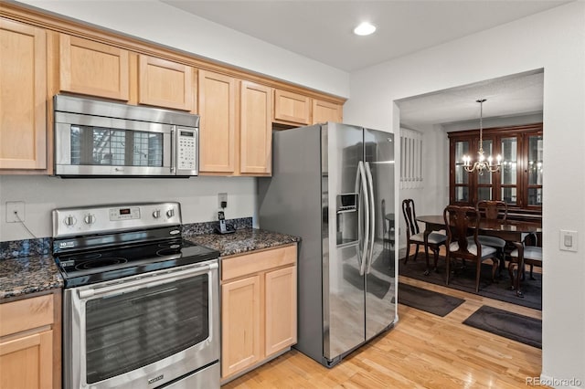 kitchen featuring appliances with stainless steel finishes, light brown cabinets, a chandelier, light wood finished floors, and dark stone countertops