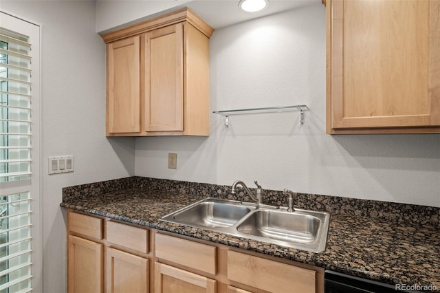 kitchen with light brown cabinetry, a sink, and dark stone countertops
