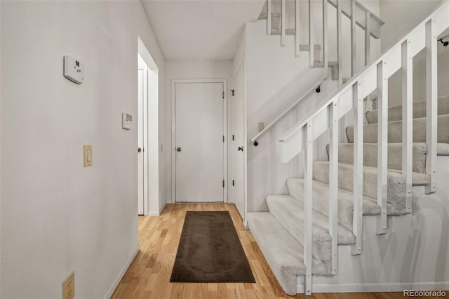 foyer entrance featuring stairs, light wood-style floors, and baseboards