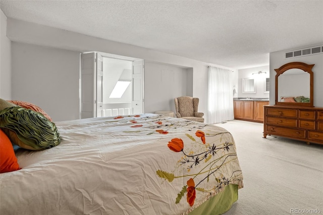 bedroom featuring light colored carpet, a textured ceiling, and connected bathroom