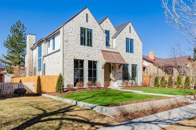 view of front of property featuring stone siding, a chimney, a front yard, and fence