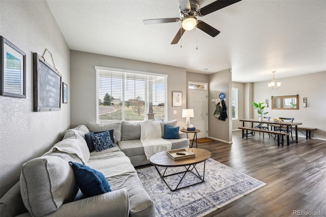 living room with dark wood finished floors, ceiling fan with notable chandelier, baseboards, and a textured wall