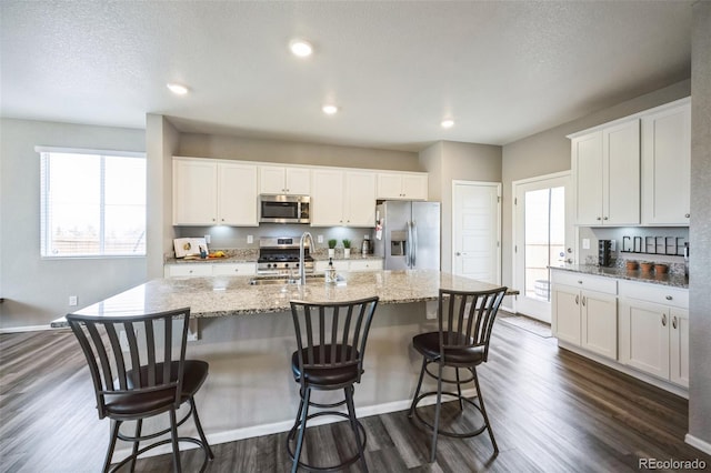 kitchen with a sink, a kitchen island with sink, appliances with stainless steel finishes, and dark wood-style floors