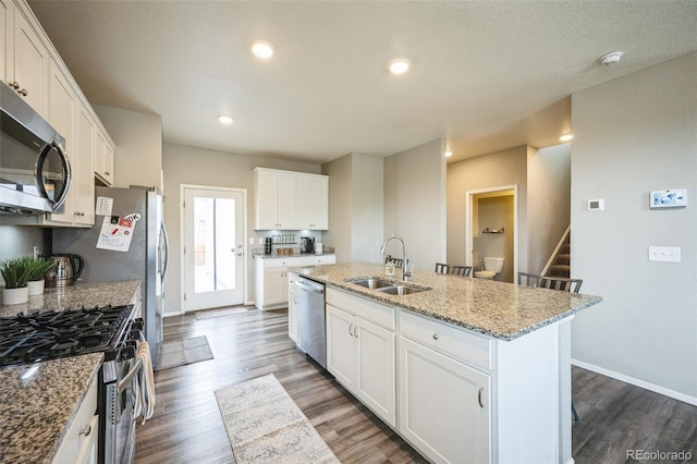 kitchen featuring dark wood-style floors, a center island with sink, a sink, appliances with stainless steel finishes, and white cabinetry