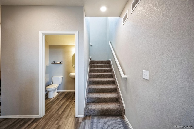 stairway featuring visible vents, baseboards, and wood finished floors