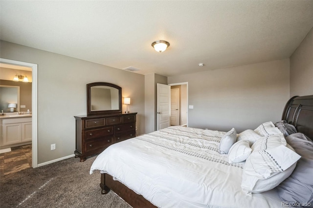 bedroom featuring visible vents, baseboards, a sink, ensuite bathroom, and dark colored carpet