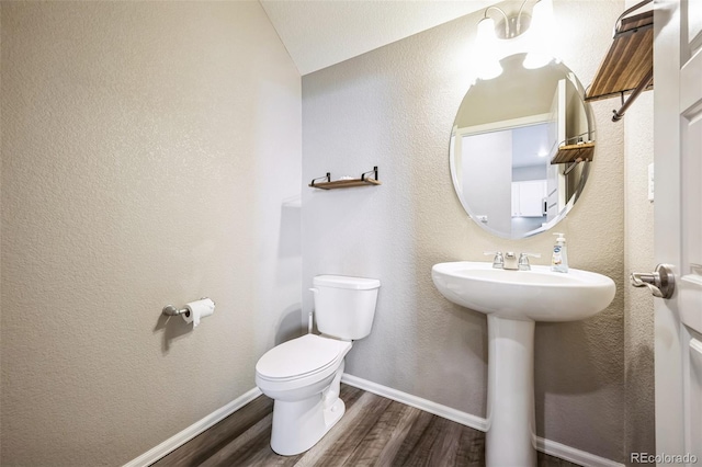 bathroom featuring toilet, a sink, wood finished floors, baseboards, and a textured wall