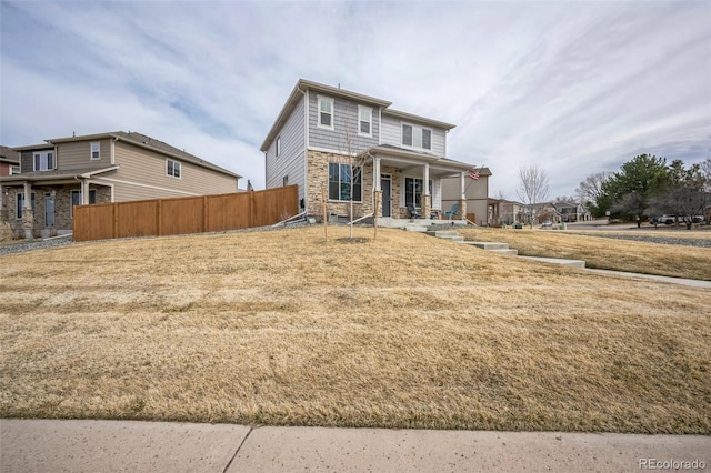 view of front of property with stone siding, a porch, a front yard, and fence